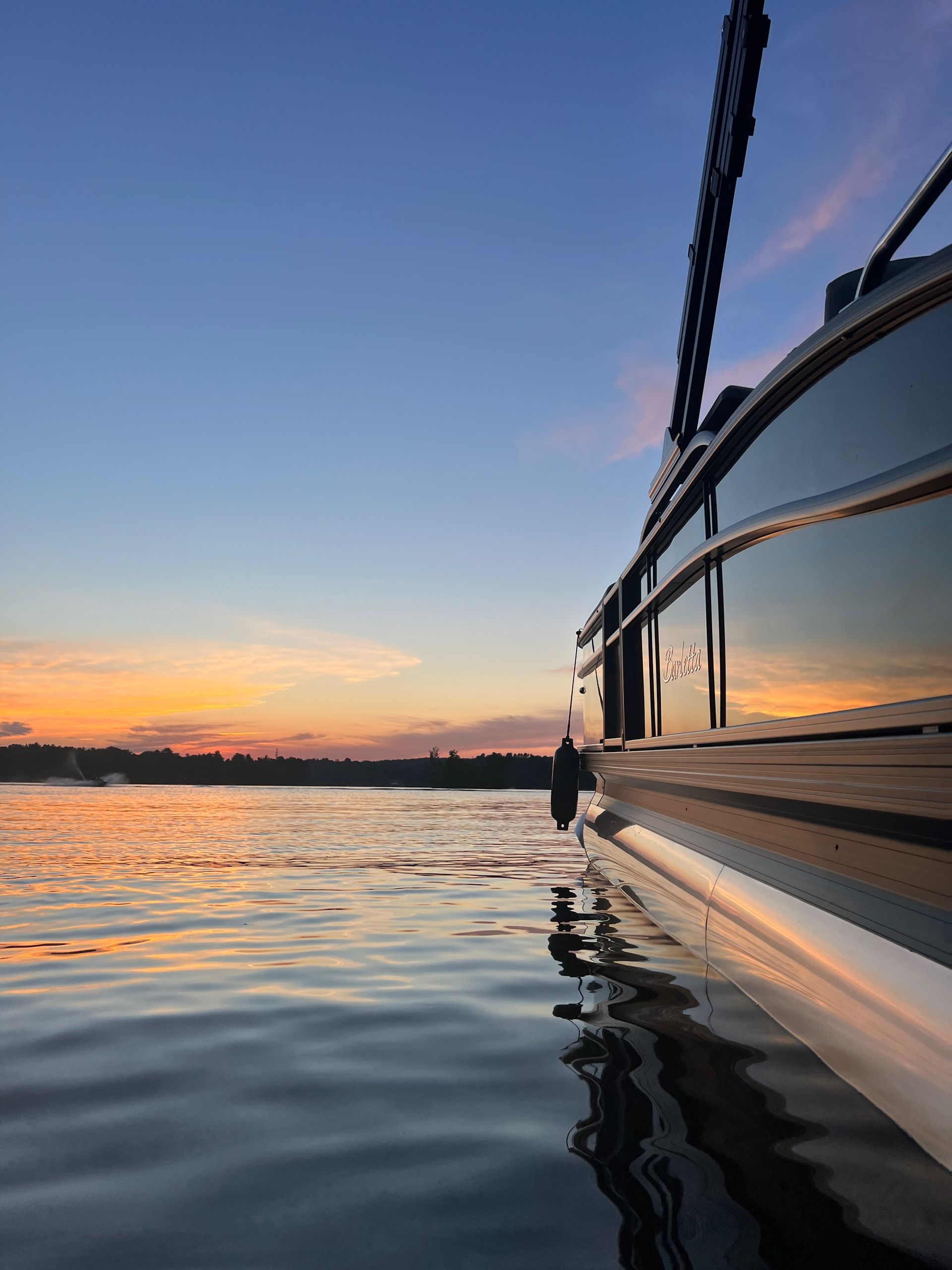 Boat on water at sunset with a reflection of orange and blue sky.