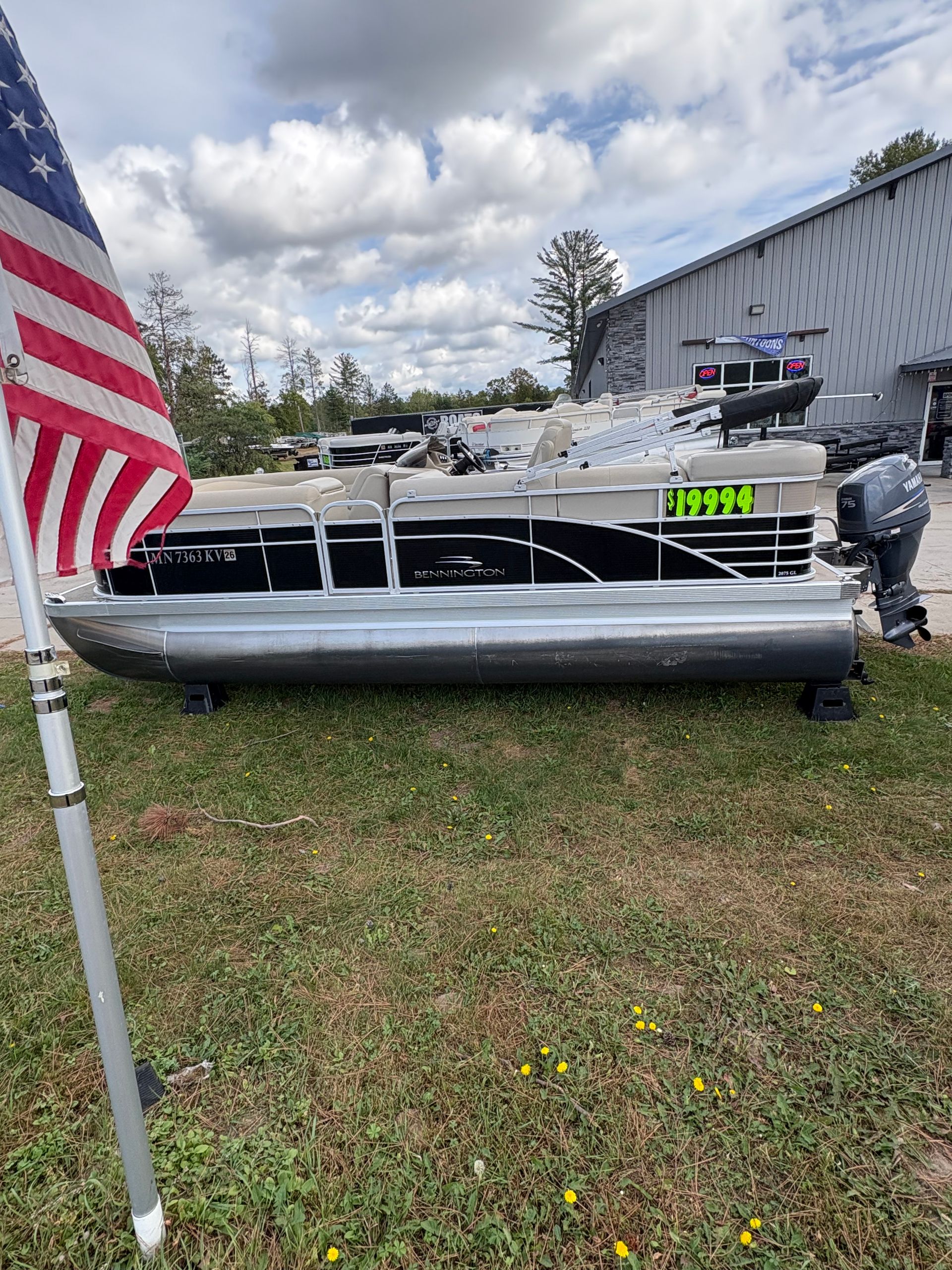 Pontoon boat on grass, American flag in foreground, building in the background.