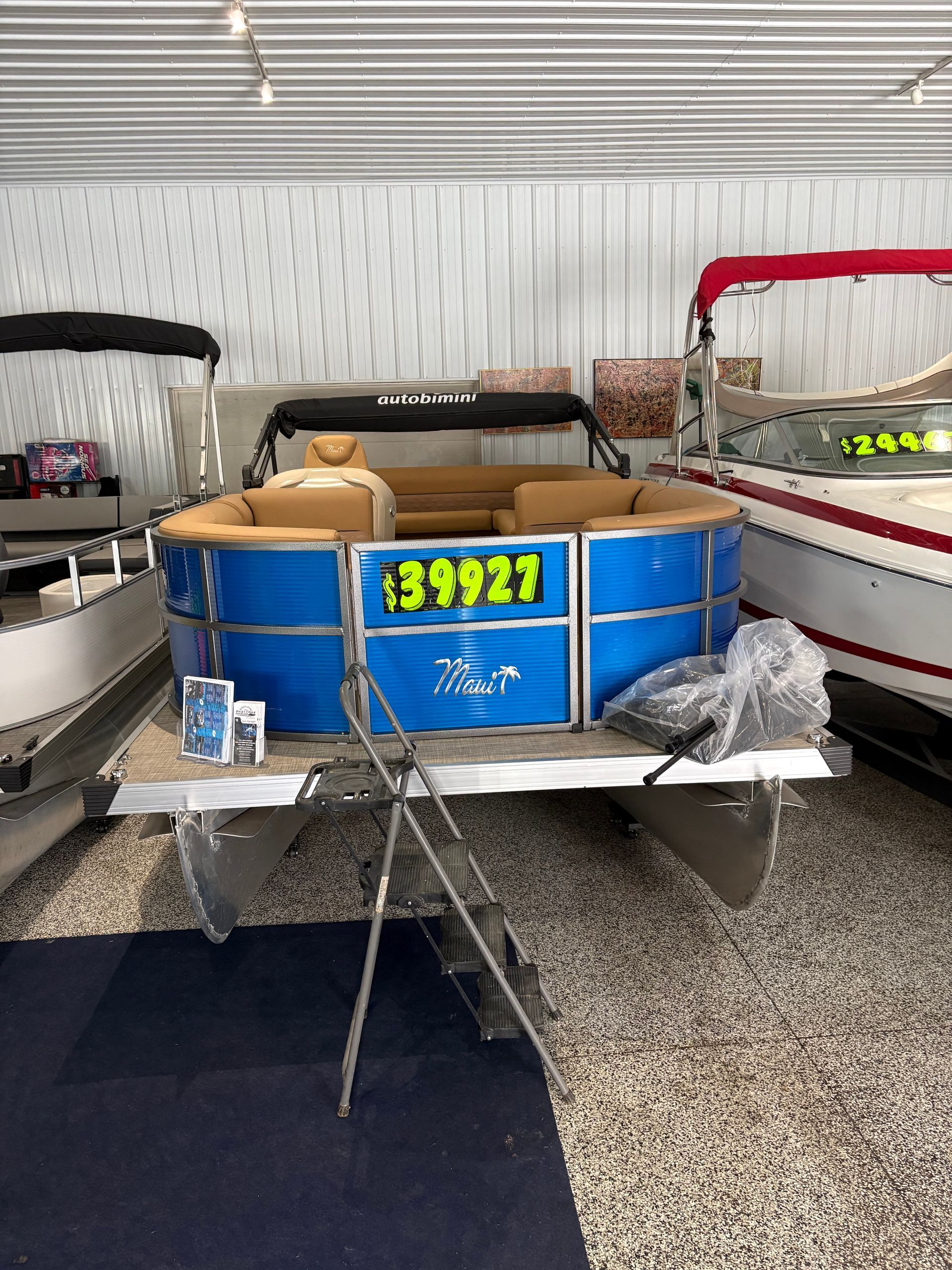Blue and tan pontoon boat with a price tag of $39,927, displayed inside a boat showroom.