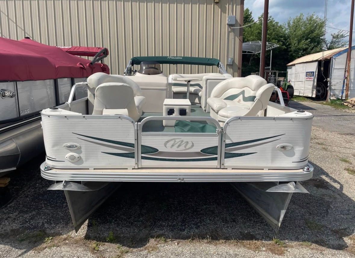 Rear view of a white pontoon boat with green accents, parked in front of a building.