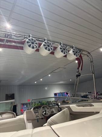 Boat interior with speakers mounted on a metal tower, white seating, and a steering wheel.