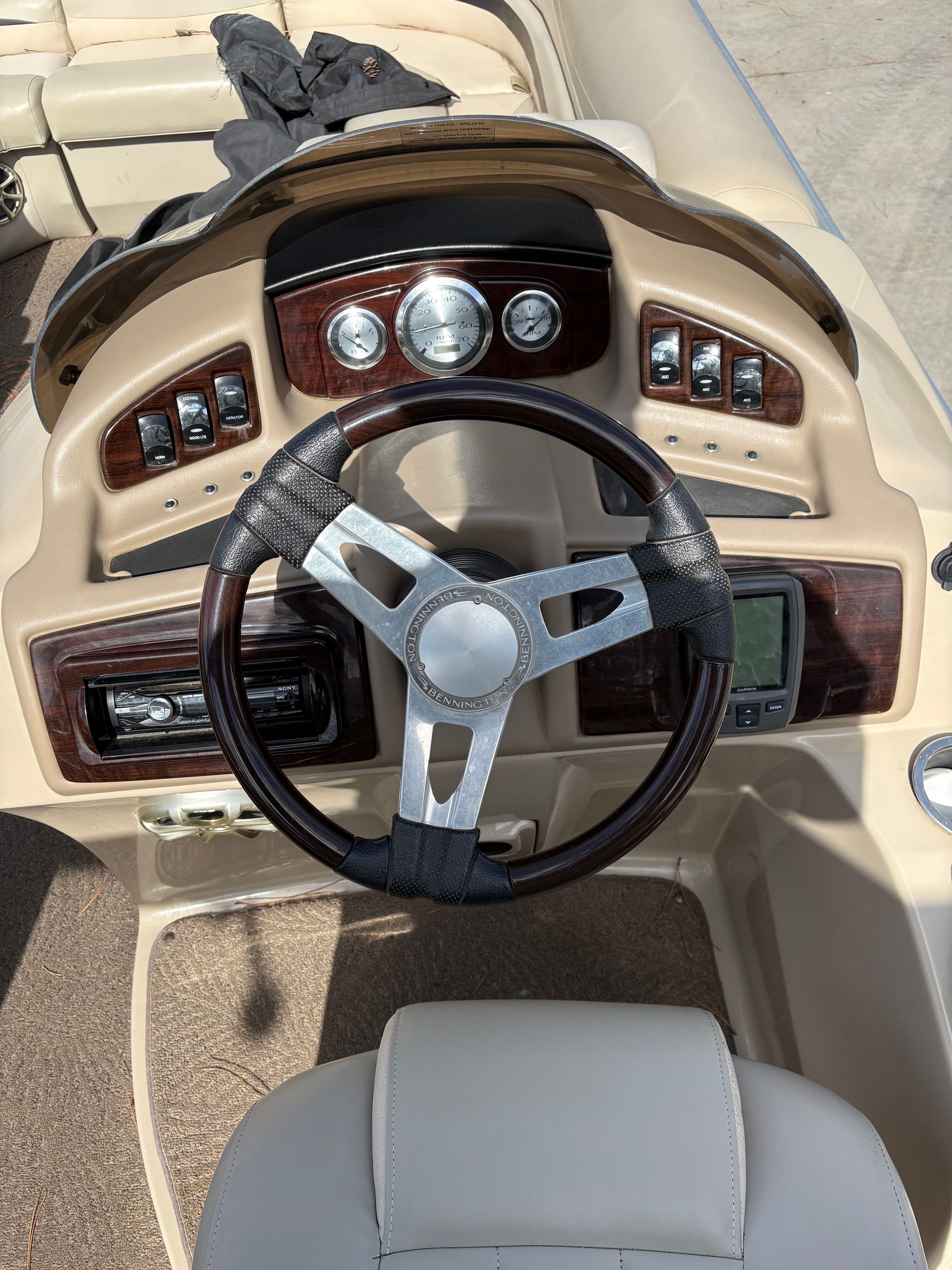 Boat dashboard with steering wheel, gauges, and switches. Tan and wood-grain accents.