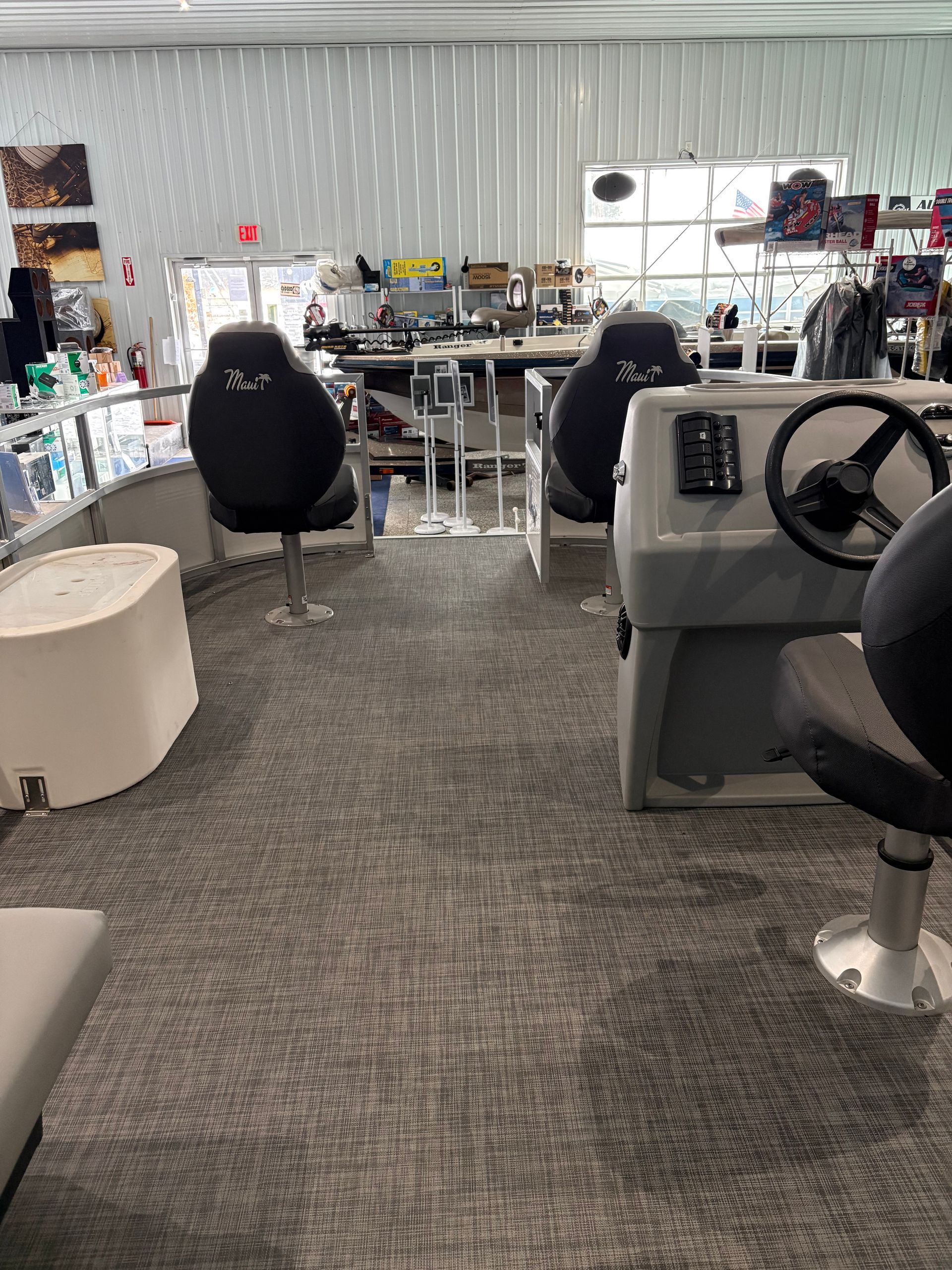 Interior of a boat showroom with gray carpet, boat seats, and equipment. Bright lighting.