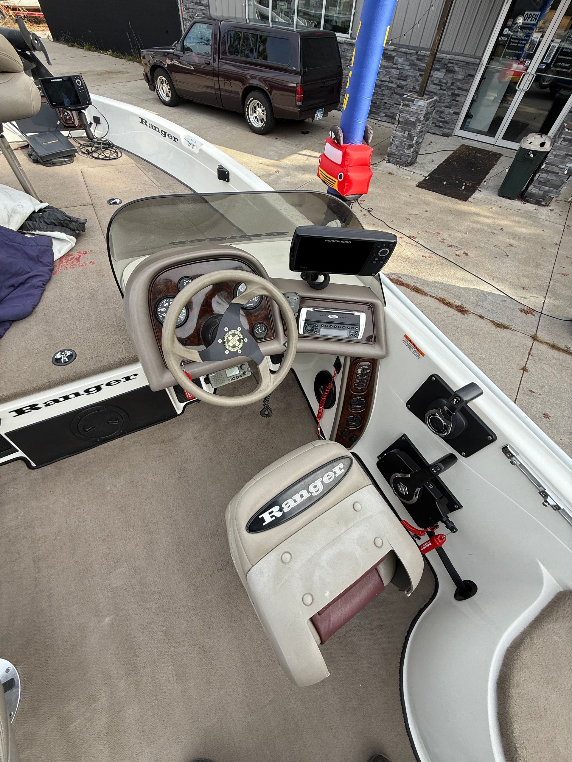 Boat interior with steering wheel, console, and driver's seat. Brown truck visible in the background.