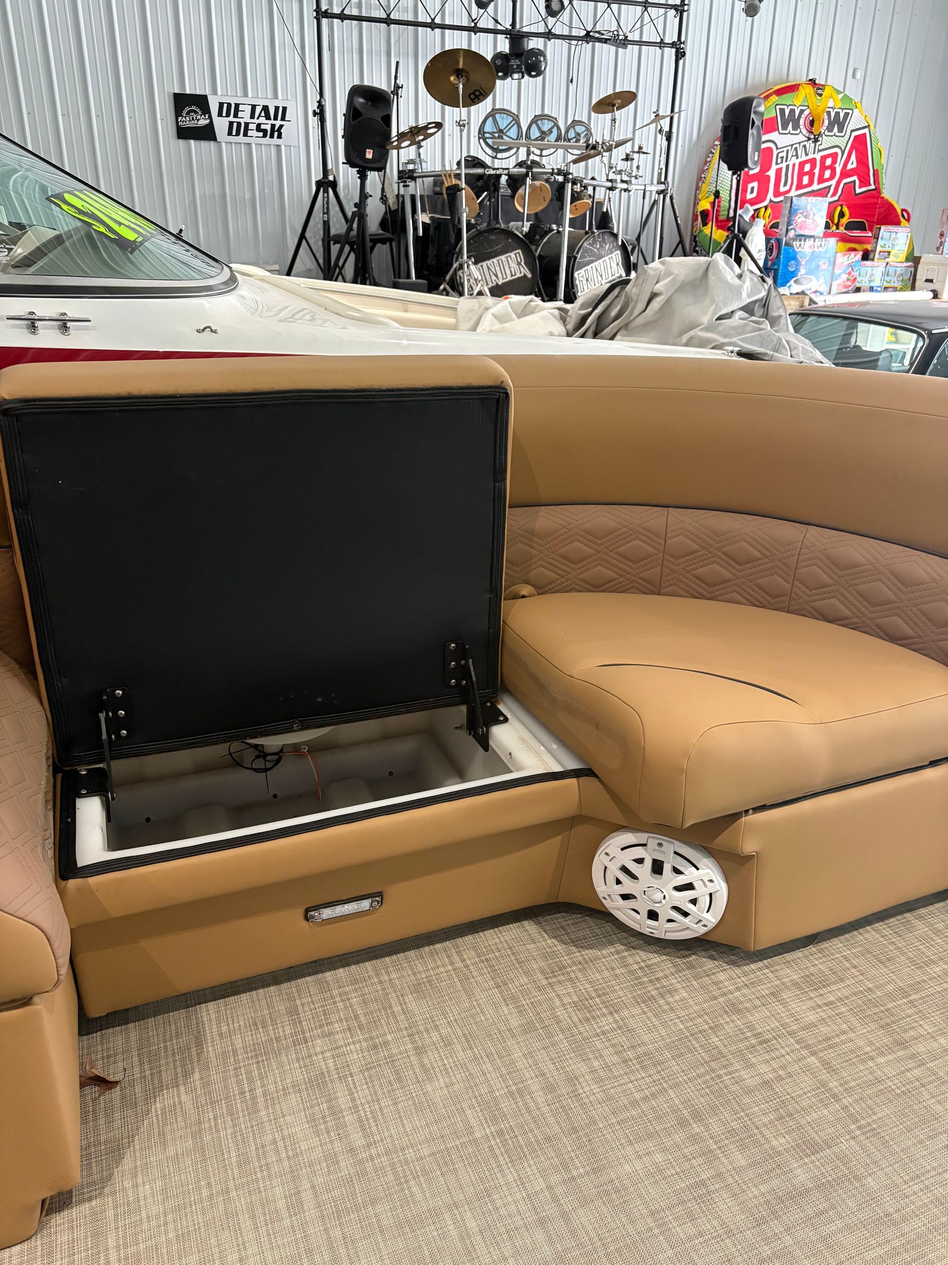 Tan boat couch with open storage, white speaker, drum set in background.
