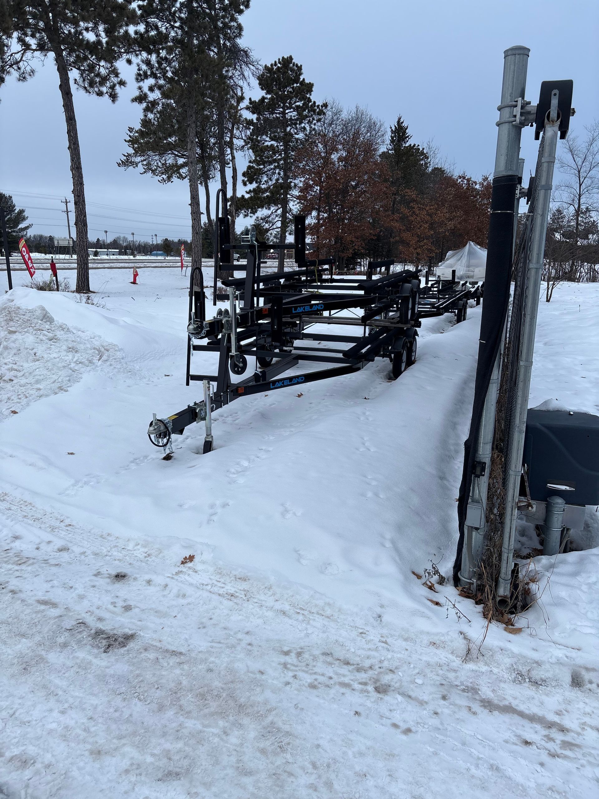 Boat trailer parked on a snow-covered hill next to a pole in a winter setting.