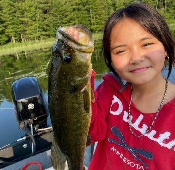 Girl in red shirt holding a large fish on a boat.