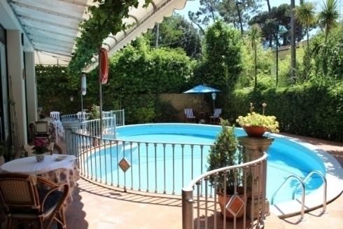 Piscina in giardino con acqua azzurra, ringhiera bianca, sedie da patio e rigogliosi alberi verdi.