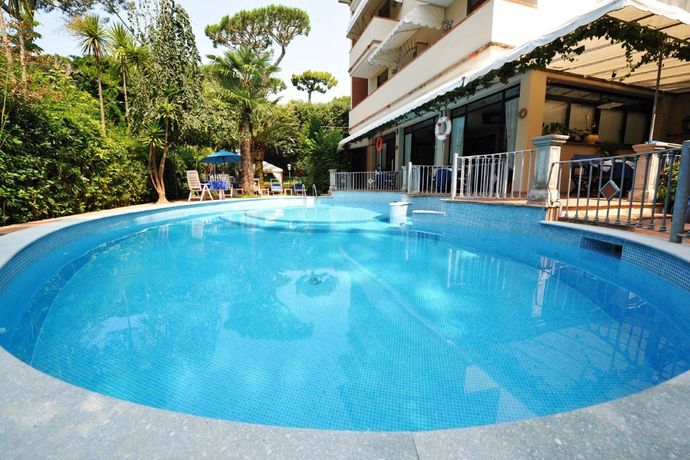 Piscina circolare blu accanto a un edificio con sedie da giardino e rigogliosi alberi verdi nelle vicinanze.