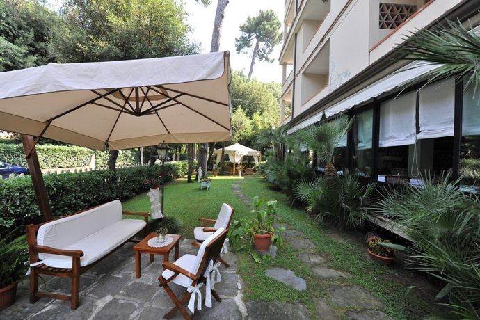 Patio esterno con ombrellone, sedie e tavolo accanto a un giardino e alle finestre dell'edificio.