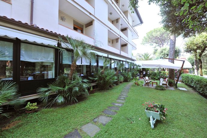 Passeggiata nel giardino accanto a un edificio bianco con finestre di vetro, prato, fiori in vaso e ombrelloni da patio.