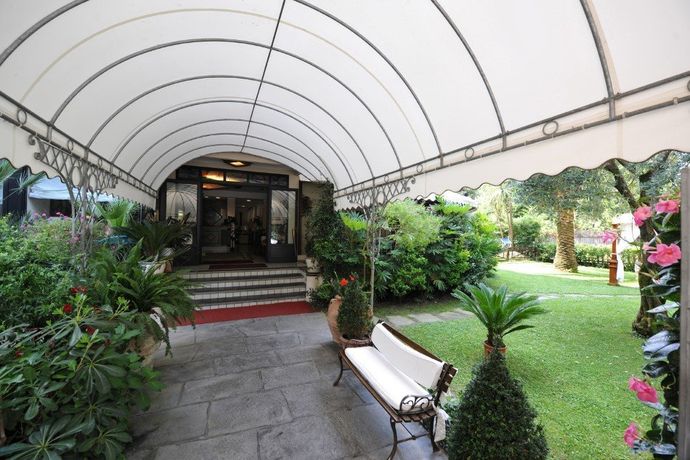 Ingresso al giardino coperto con tettoia bianca, sentiero in pietra, scalini, panchine e vegetazione lussureggiante.