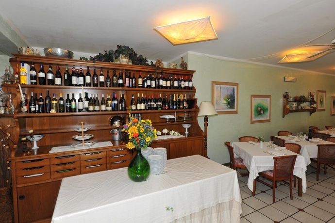 Sala da pranzo del ristorante con scaffali in legno al bancone, tovaglie bianche e luci calde sul soffitto.