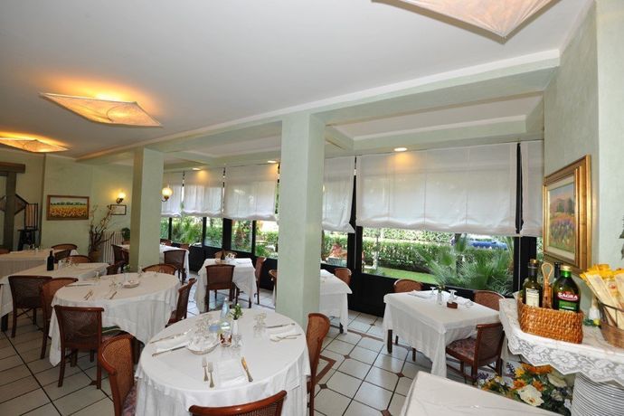Elegante sala da pranzo con tovaglie bianche, pavimento piastrellato e ampie finestre che si affacciano sul verde.