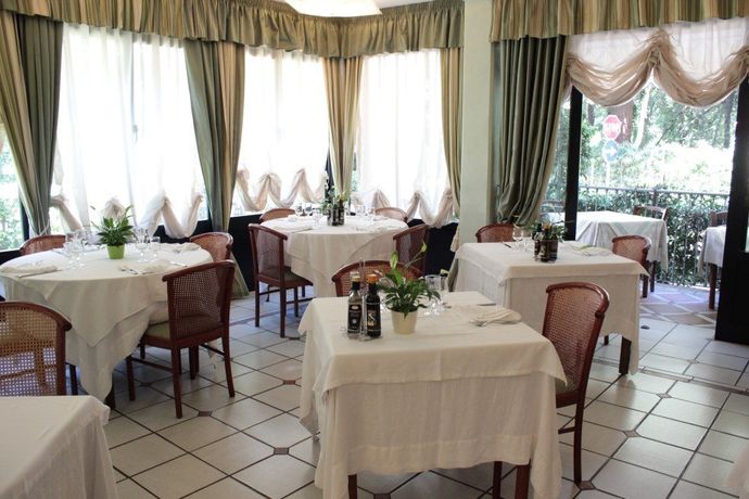 Luminosa sala da pranzo del ristorante con tovaglie bianche, sedie in vimini e grandi finestre con tende.
