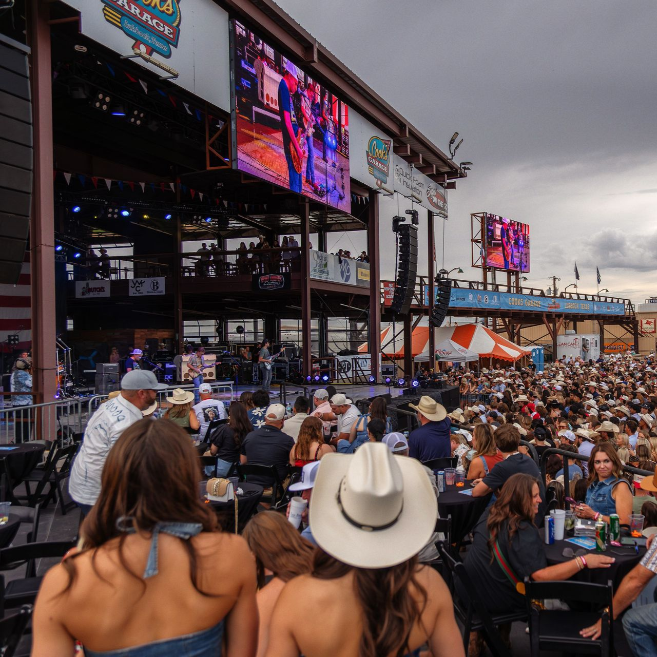 Large outdoor concert with stage, crowd of people, and large screens.