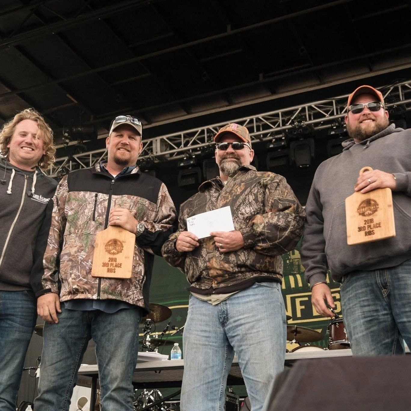 Four men on stage at an event, holding awards and a check.