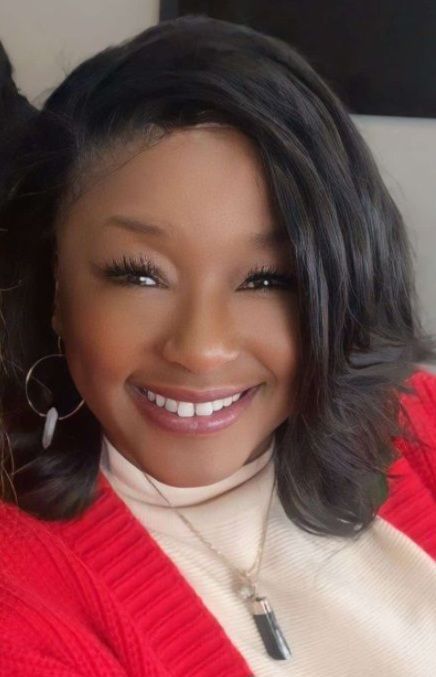Woman smiling, wearing a red sweater and beige turtleneck, with a necklace.