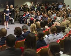 Woman in blue dress speaks at podium to large audience in a theater.