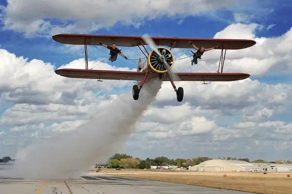 A red biplane is taking off from an airport runway