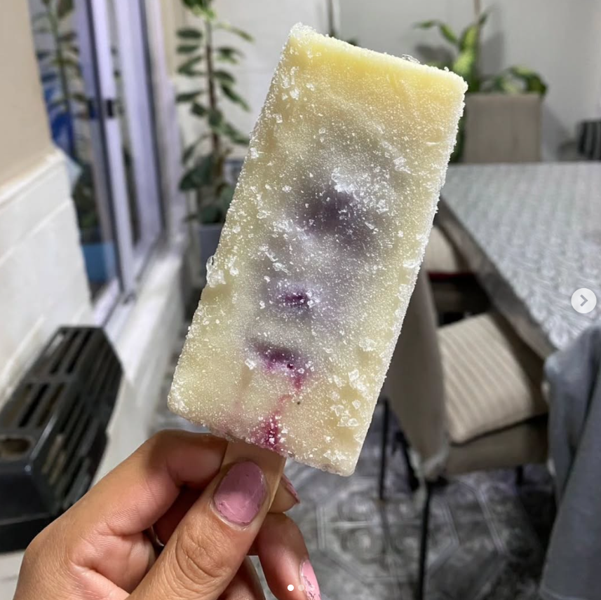 Persona que sostiene una paleta blanca con trozos de fruta morada visibles, contra un fondo interior borroso.