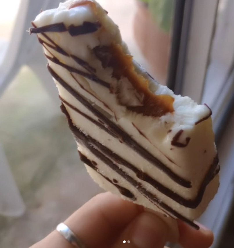 Una mano que sostiene una barra de postre blanca, parcialmente comida, rociada con chocolate negro.