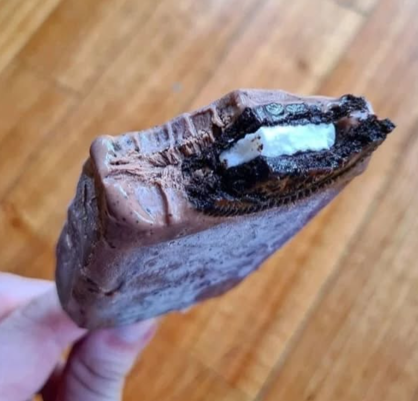 Mano sosteniendo un sándwich de helado parcialmente comido con una galleta Oreo dentro.