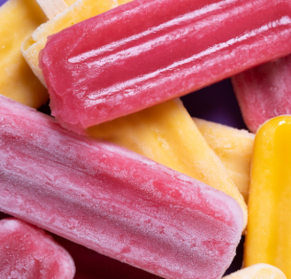 Paletas heladas de colores, rosas y amarillas, apiladas sobre una superficie violeta.