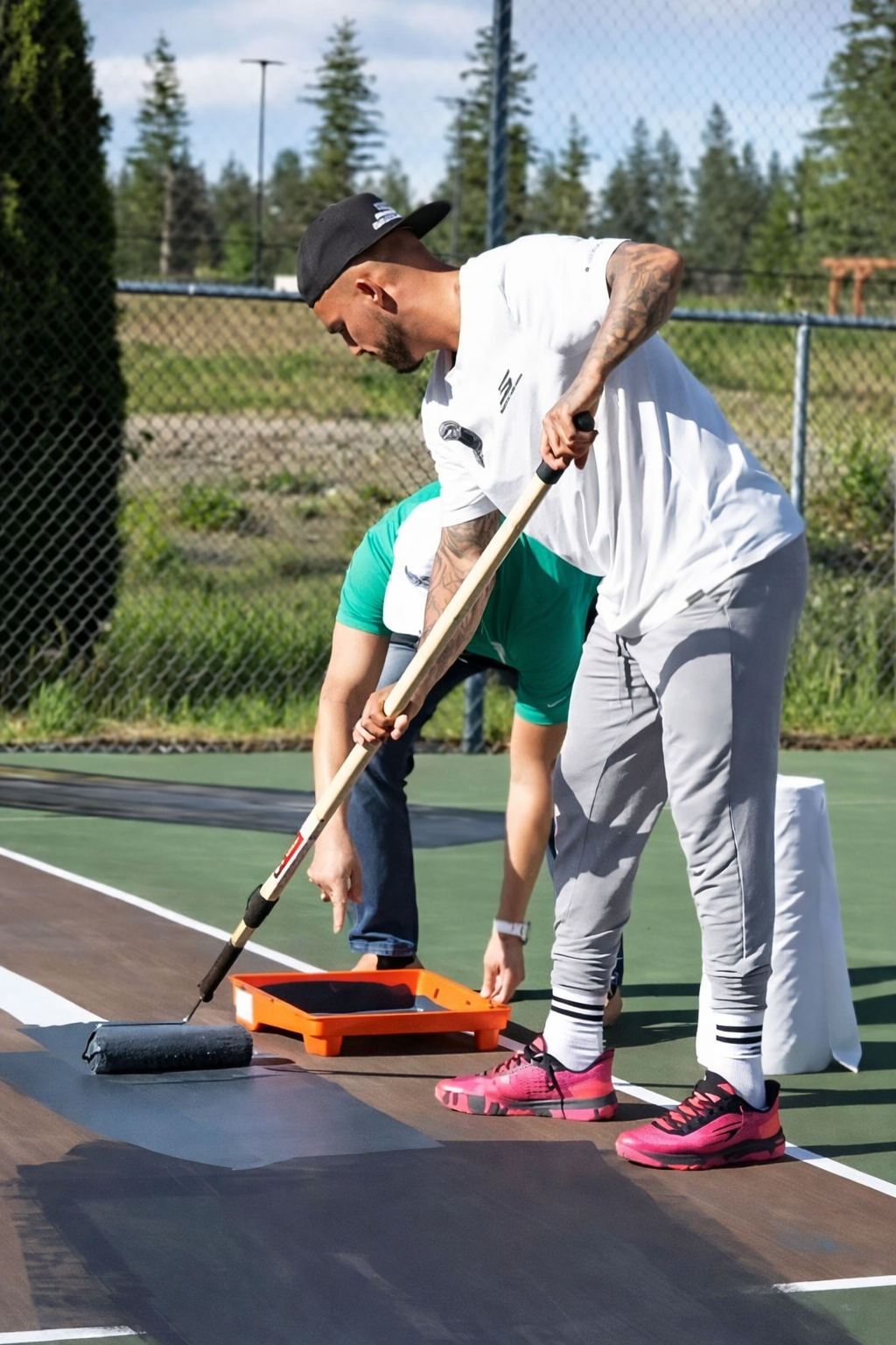 Person painting a white line on a tennis court, wearing a respirator, safety gloves, and RiteWay shirt.