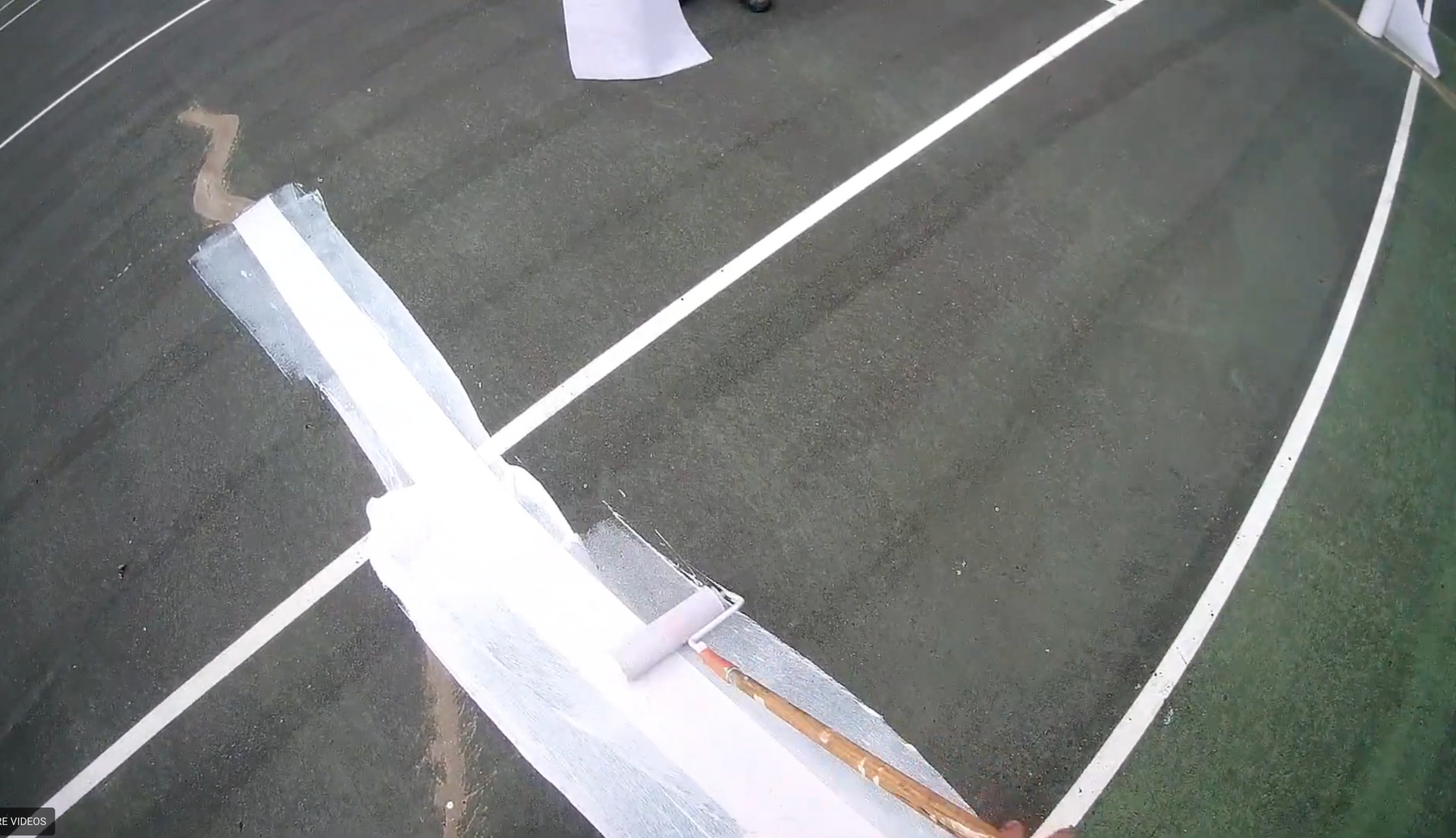 Person painting a white line with a roller over a crack in a blue tennis court, using RiteWay tape.