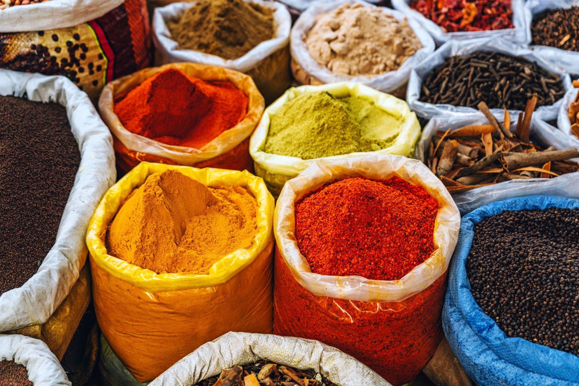 Bags filled with colorful spices, including red, yellow, and green powders, in a market setting.