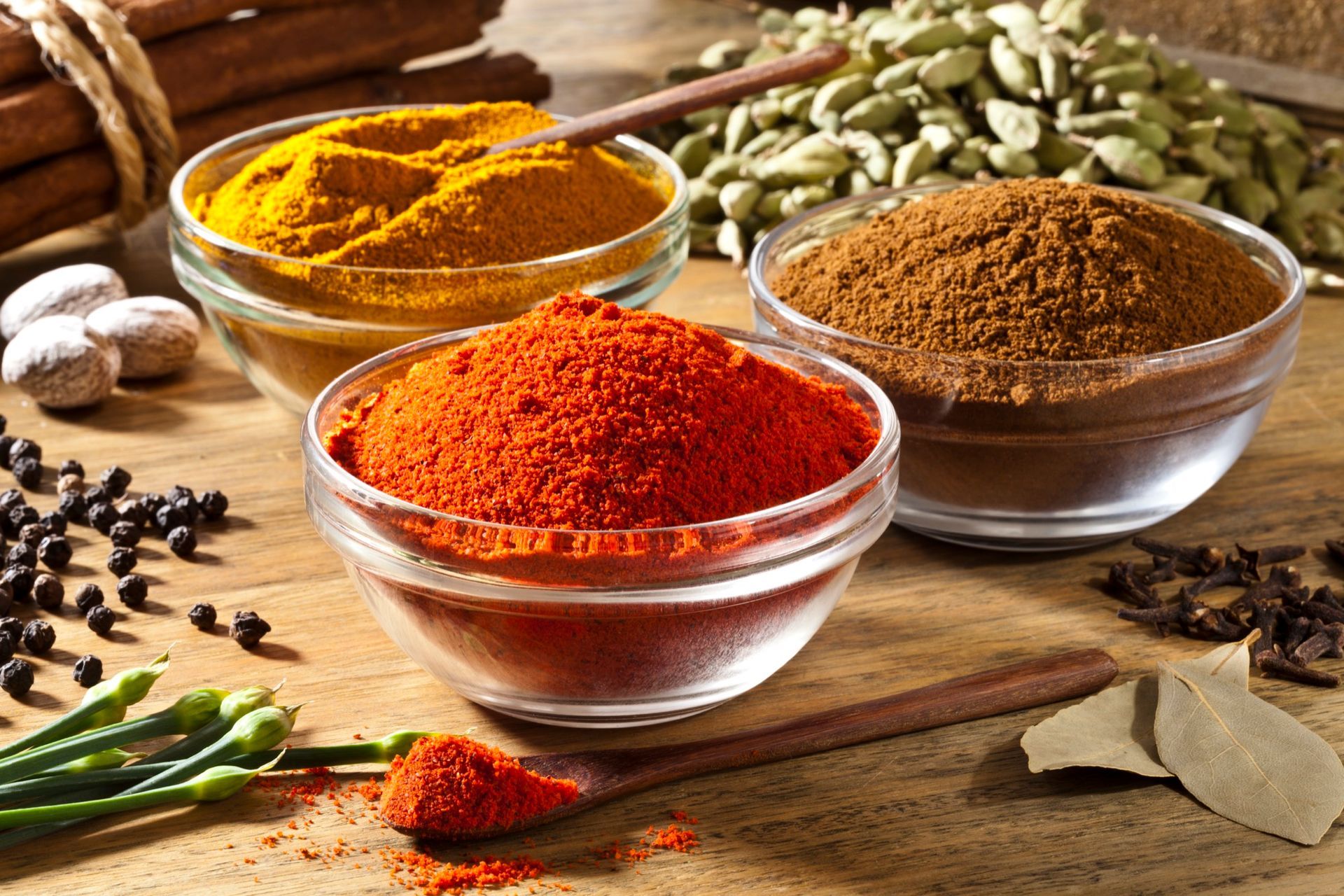 Bowls of spices: paprika, turmeric, and brown spice. Also, cinnamon sticks, peppercorns, cardamom, nutmeg, and bay leaves.