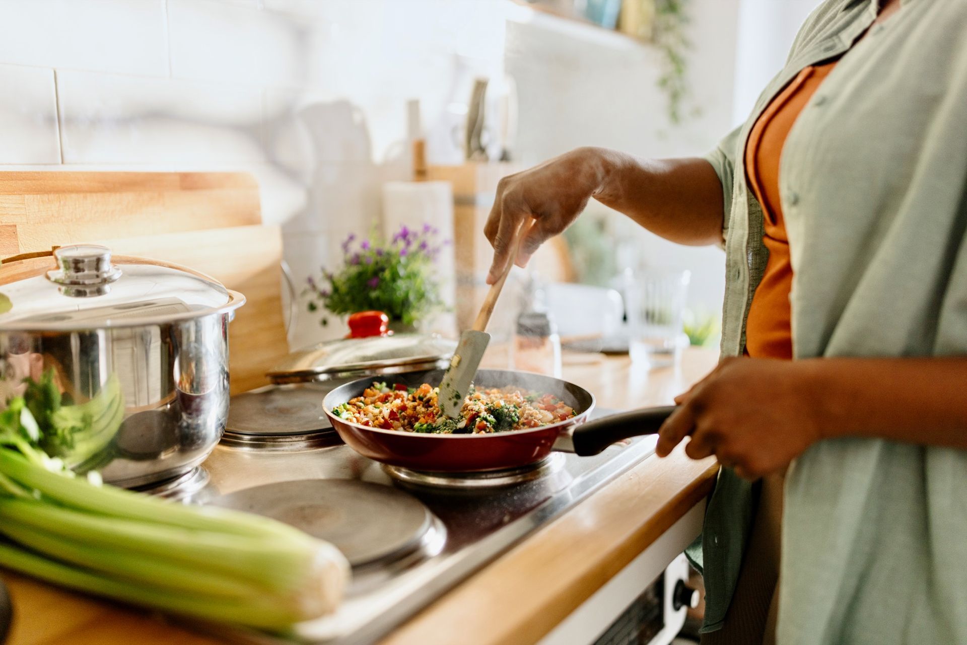 Person cooking in kitchen, stirring food in a red pan on the stove with a spatula.
