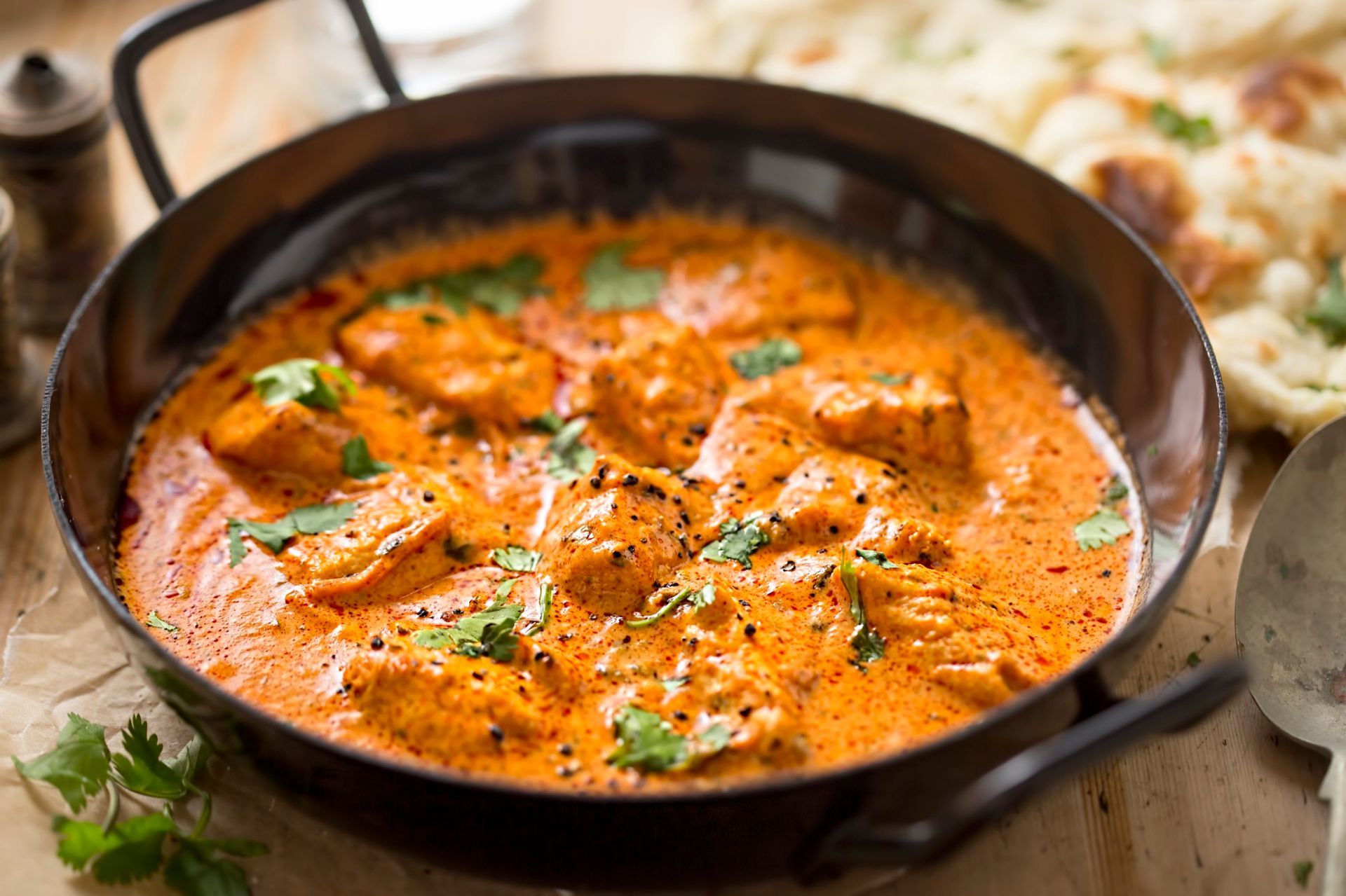 Chicken tikka masala in a copper pan with cilantro garnish, served with naan bread.