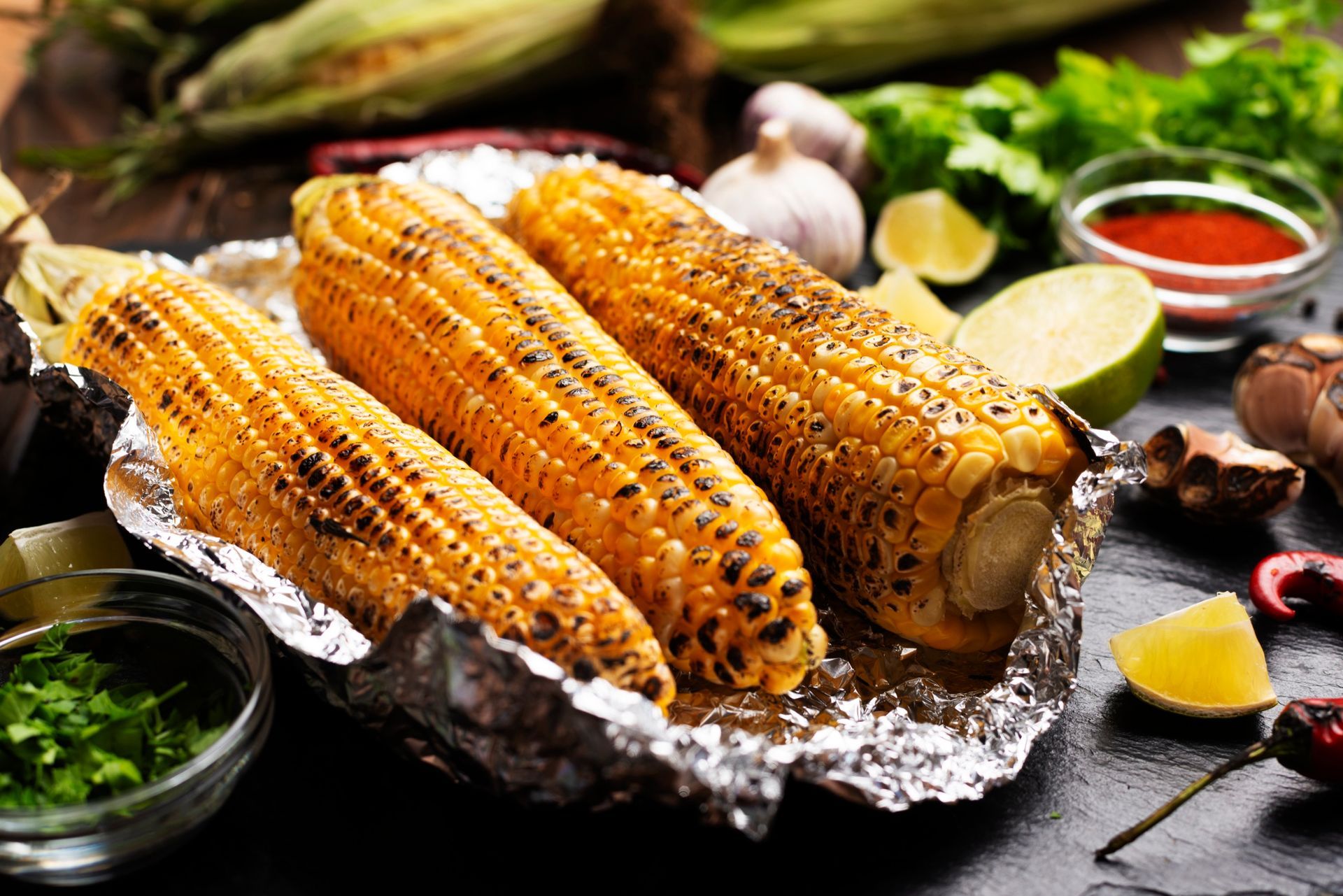 Grilled corn on the cob on foil with lime, spices, and garlic.