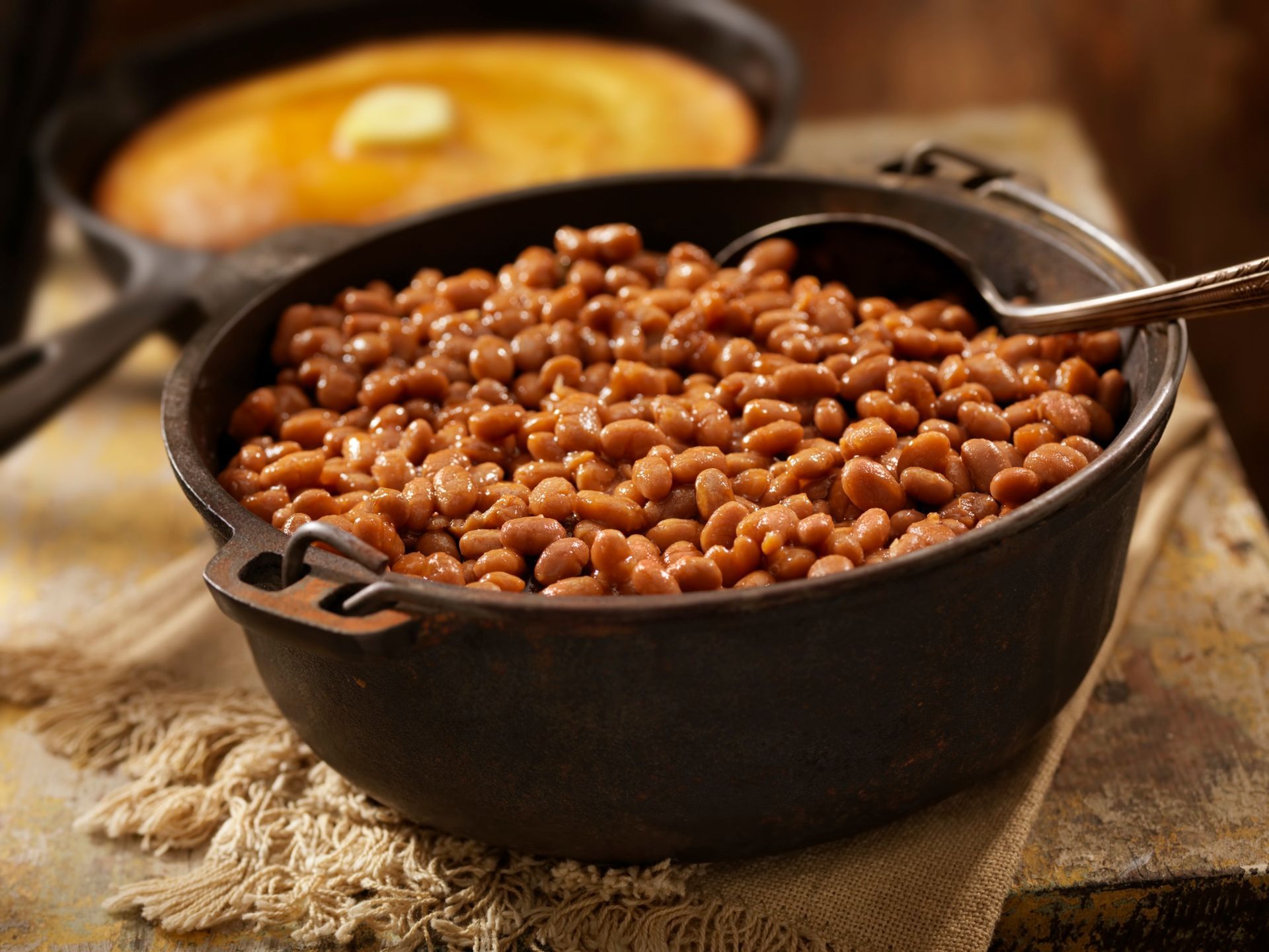 Bowl of baked beans with cornbread in background.