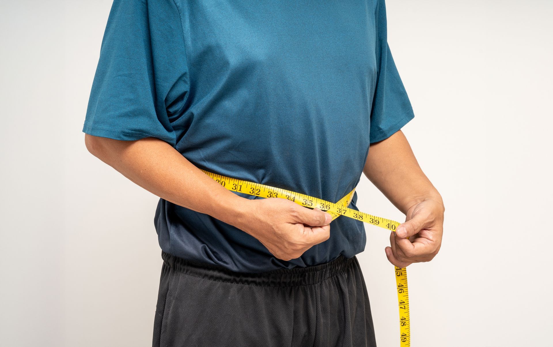Person measuring waist with a yellow tape measure while wearing green workout clothes