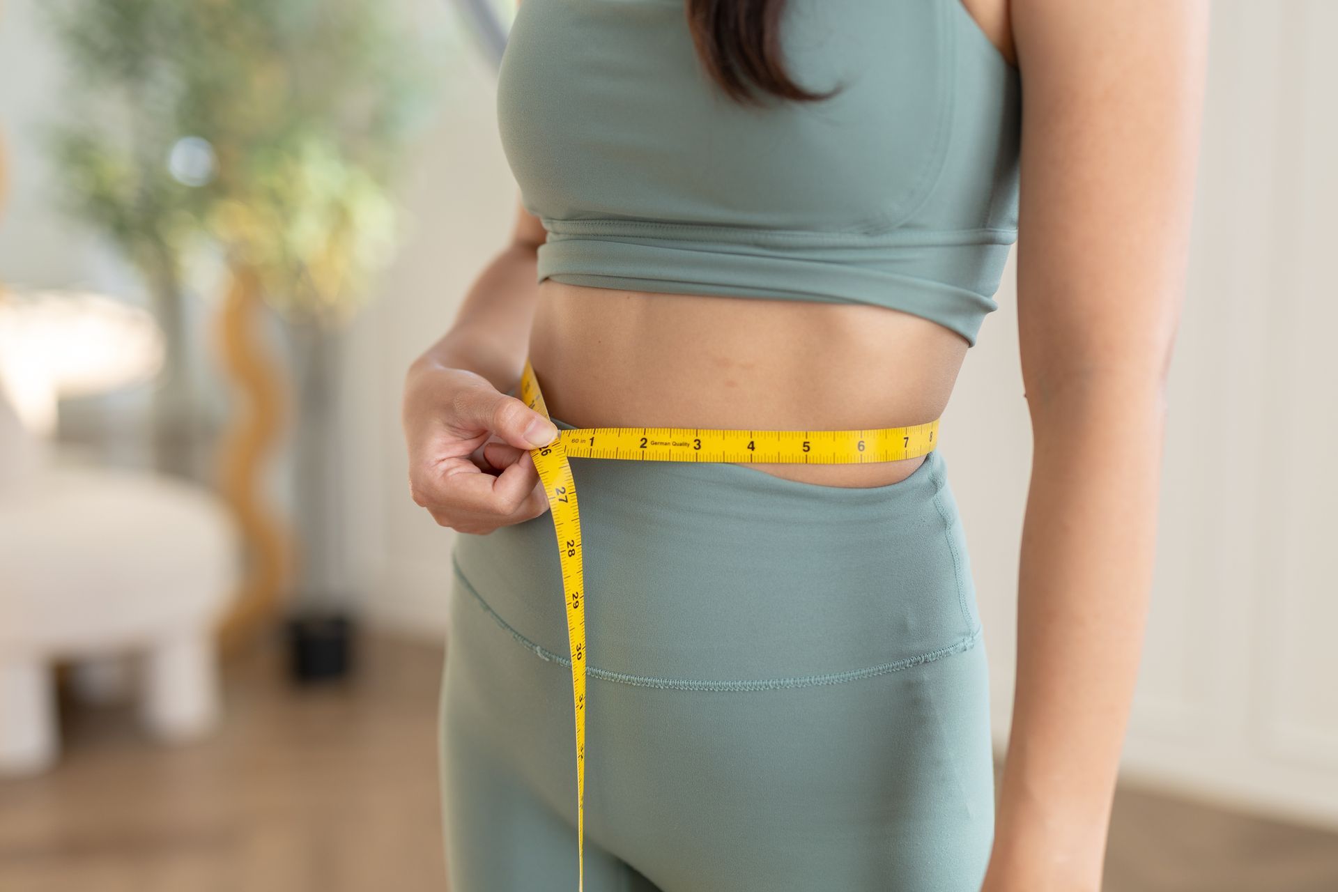 Person measuring waist with a yellow tape measure while wearing green workout clothes