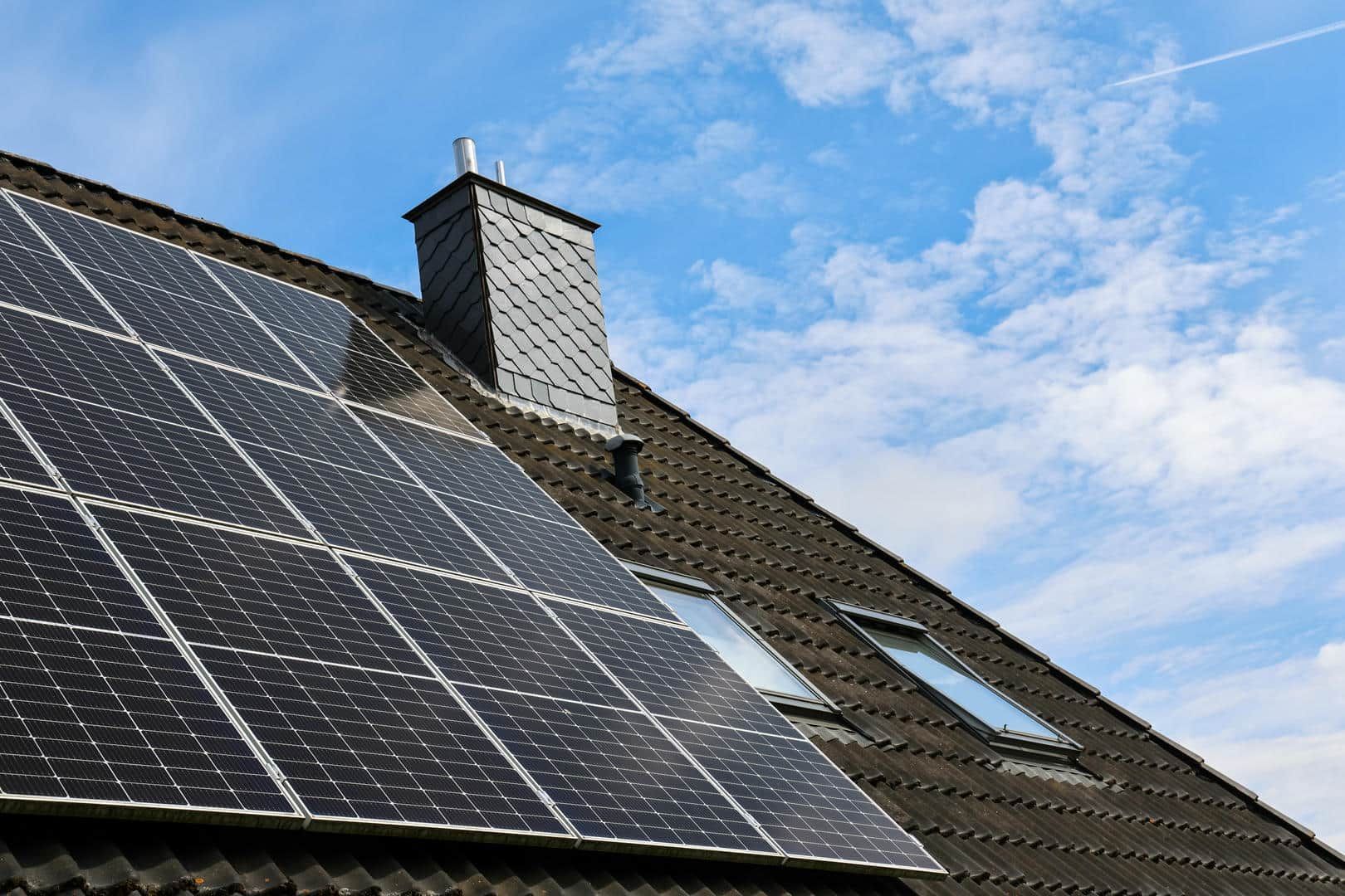 There are many solar panels on the roof of a house.
