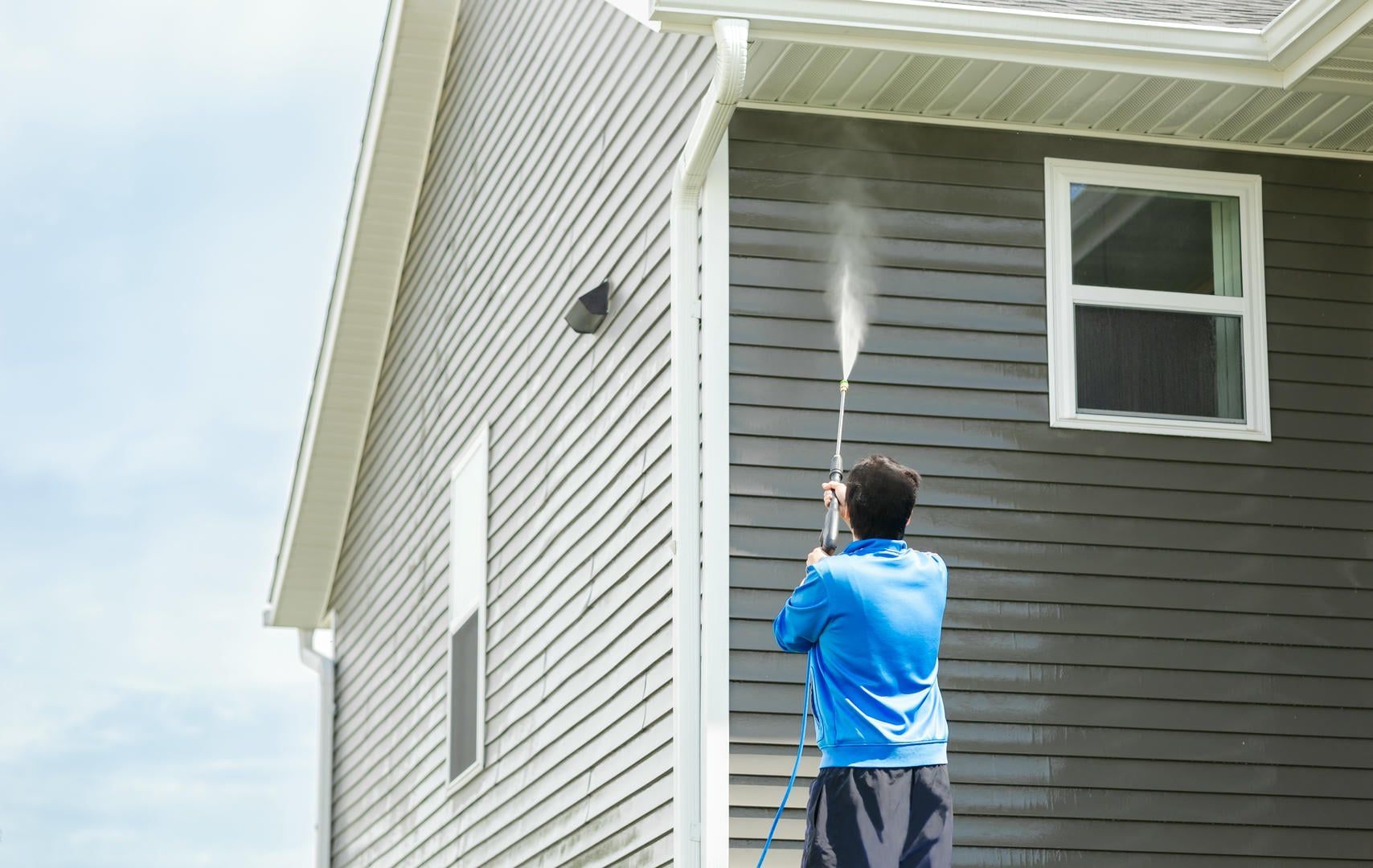 A man is cleaning the side of a house with a pressure washer.