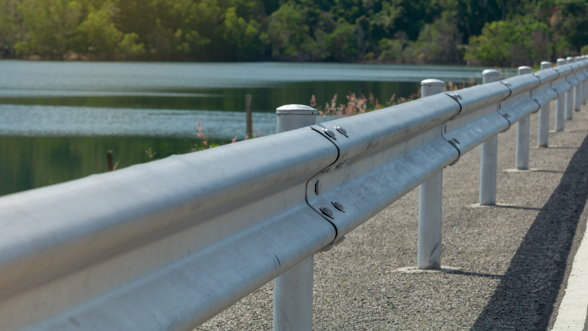 a metal railing on a highway next to a lake .