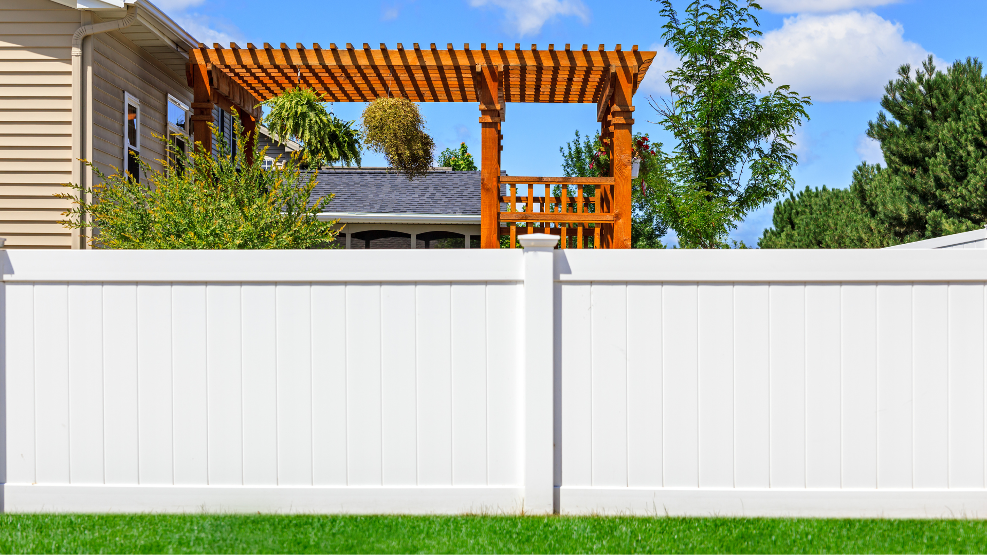 a white fence with a wooden pergola in the backyard of a house .