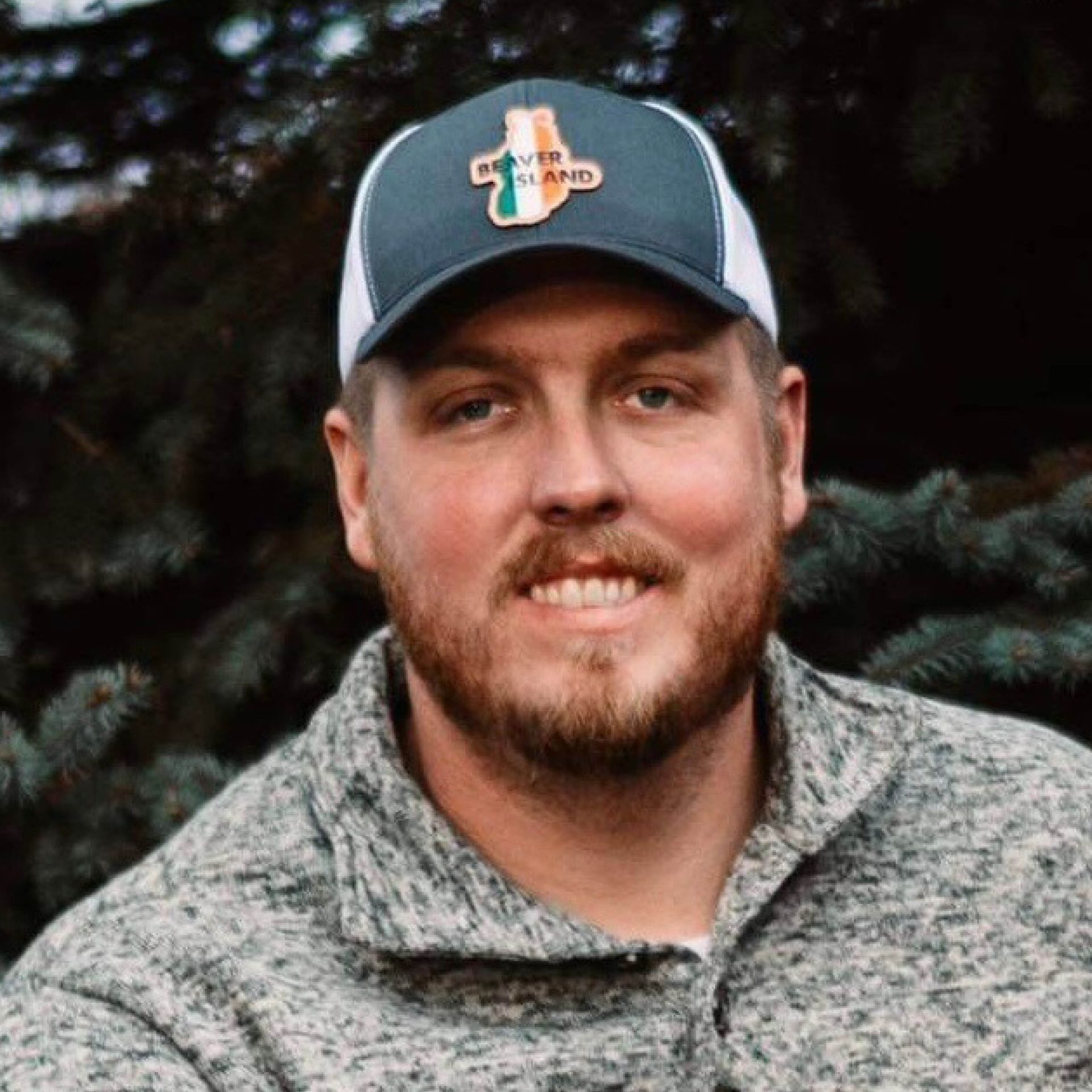 Ryan Montague with a beard is wearing a baseball cap and a sweater.