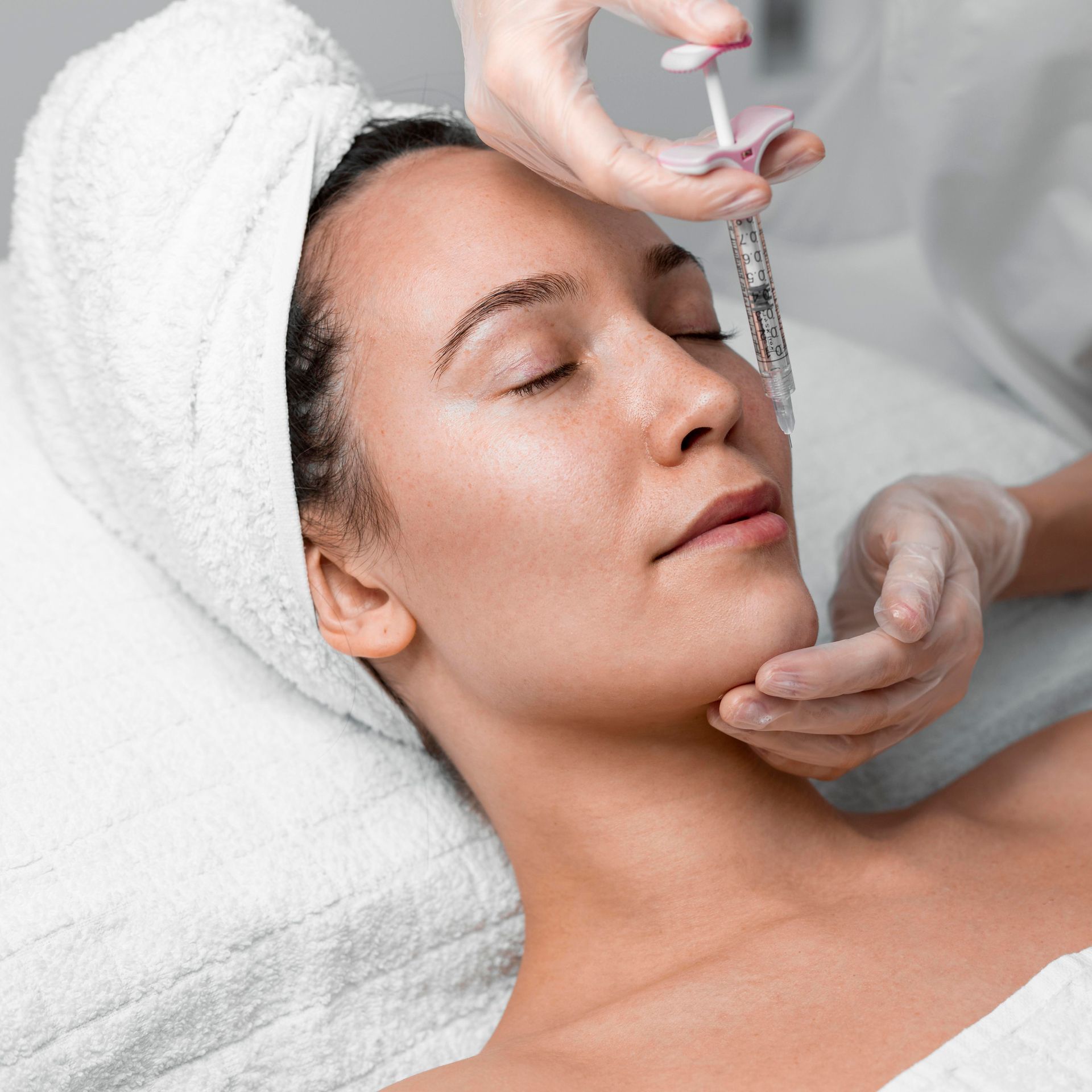 A woman with a towel wrapped around her head is getting a facial treatment.