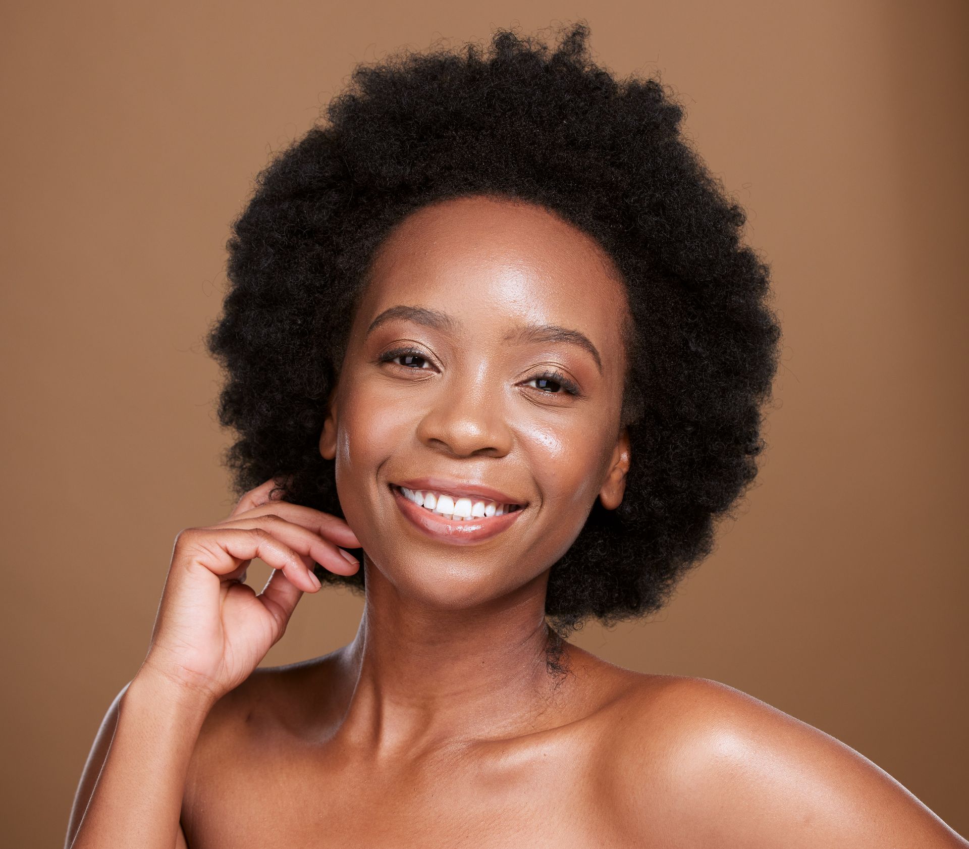 A woman with an afro is smiling and touching her face.
