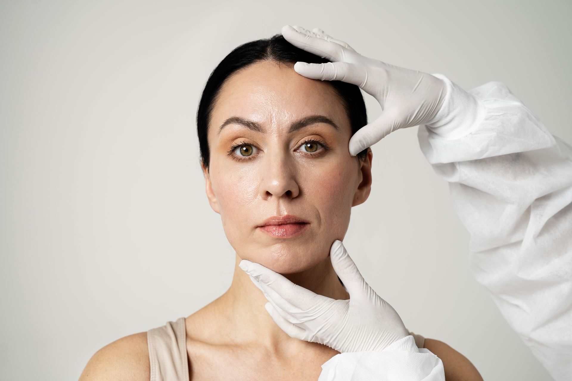 Doctor examining a woman's face with gloved hands.