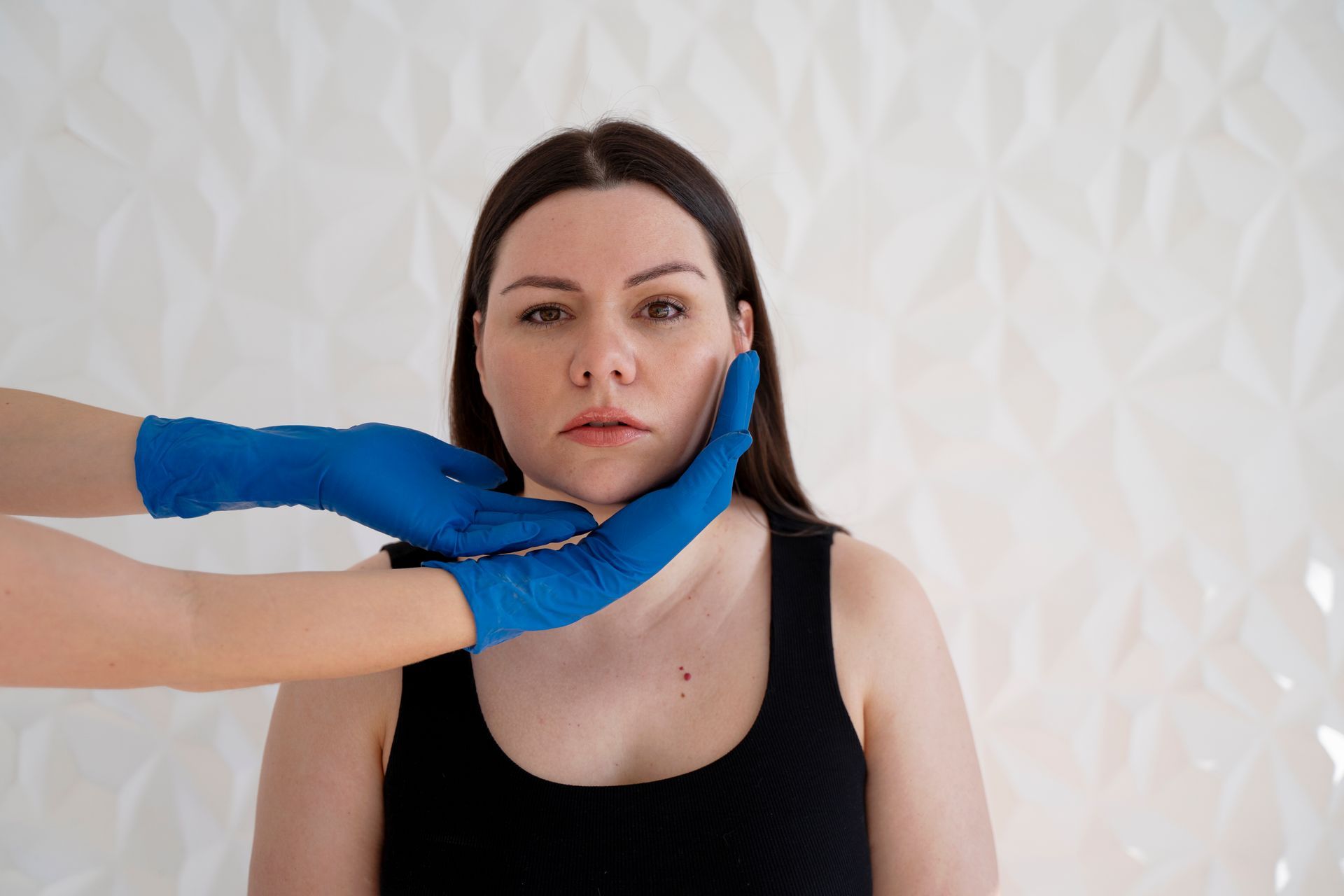 A woman is getting her face examined by a doctor wearing blue gloves.