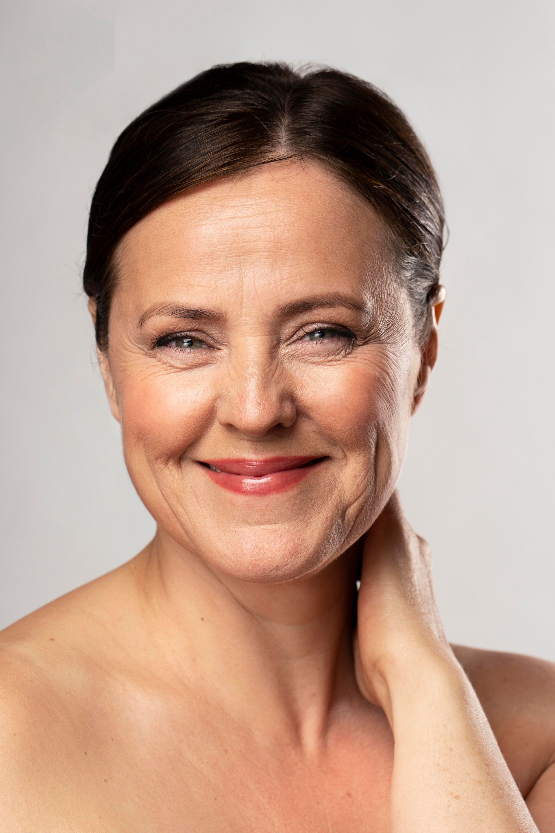 A woman is smiling and touching her neck with her hand.