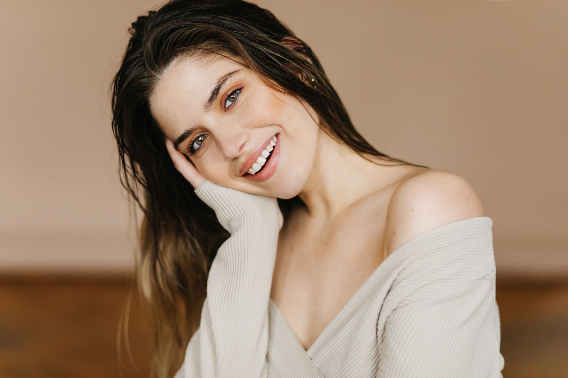 A woman is smiling and touching her face with her hand.