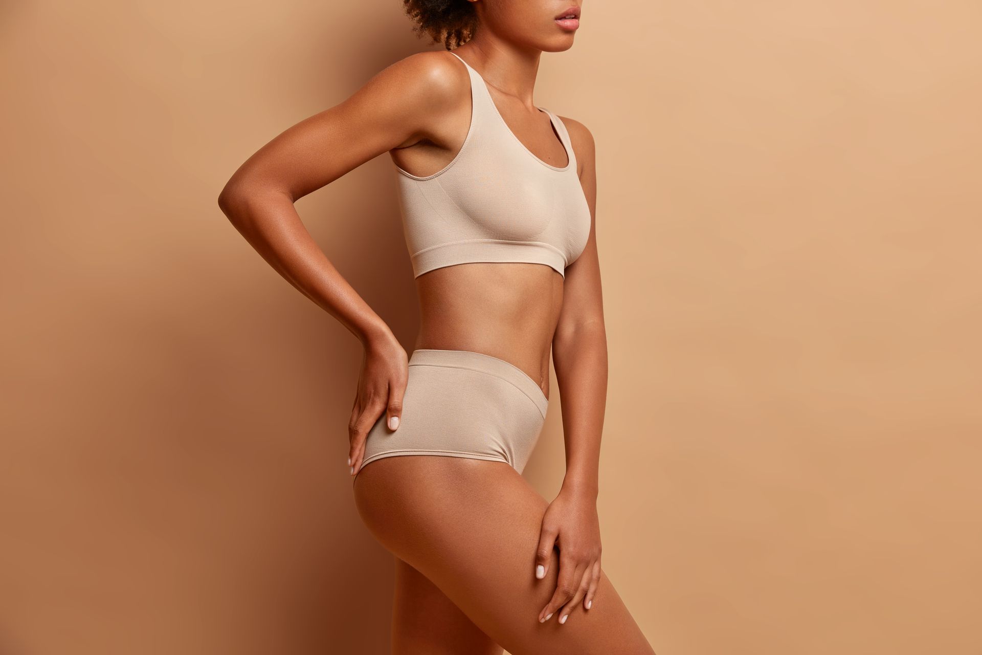 A woman in a white sports bra and shorts is standing with her hands on her hips.